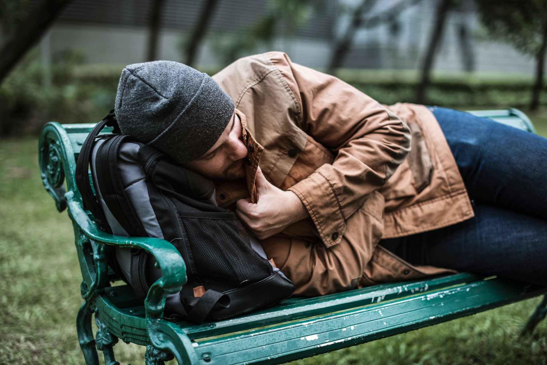 A man is sleeping on a park bench with a backpack.