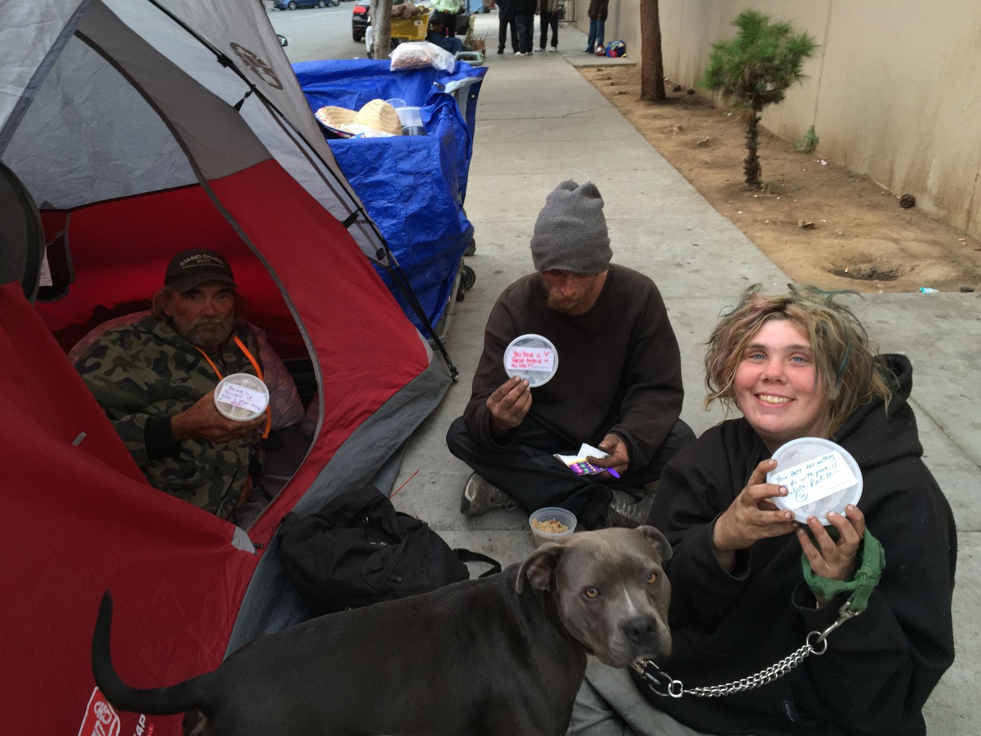 A group of people are sitting on the sidewalk eating food